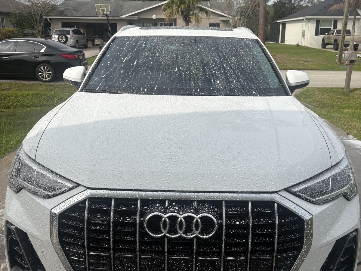 White Audi Q3 mid-wash with water beading across the hood