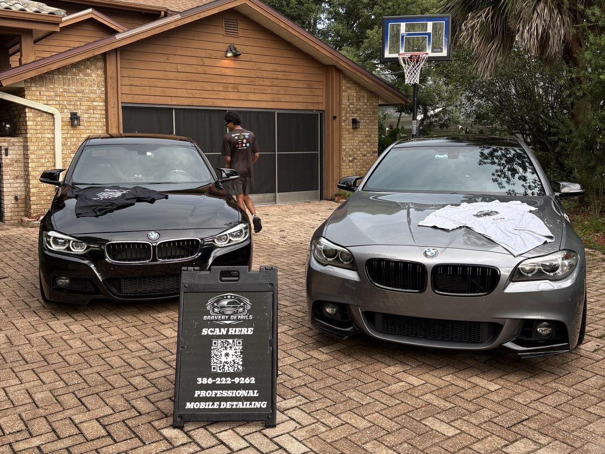 Black BMW 3 Series and grey 5 Series detailed together in a driveway, Bravery Details sign between them
