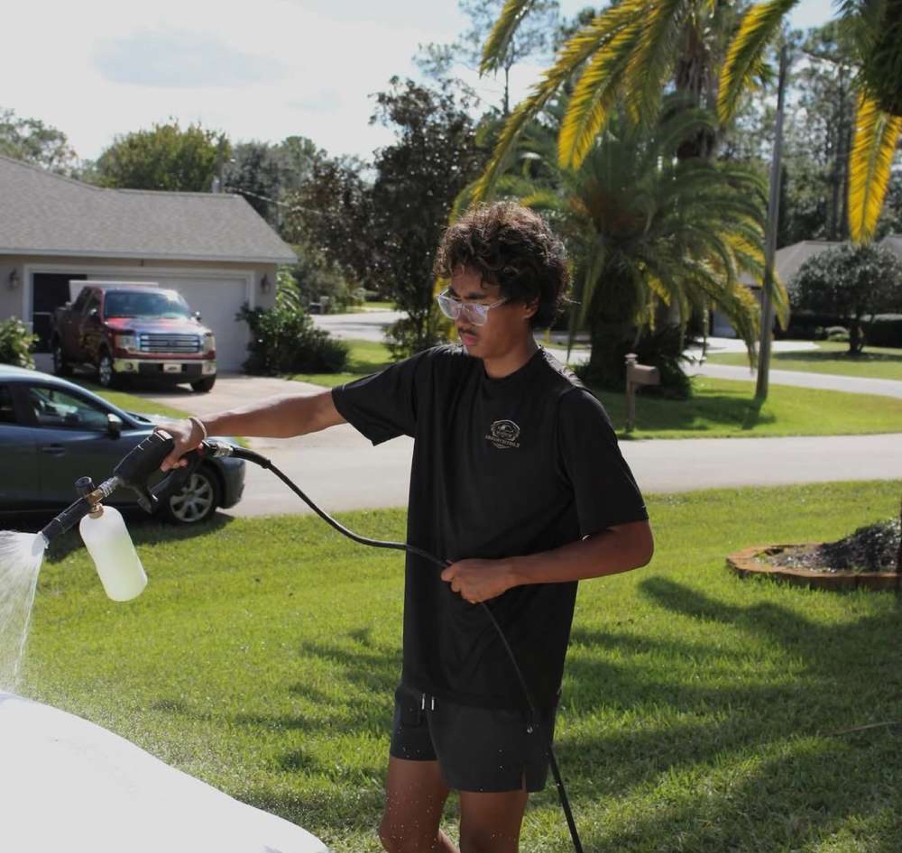 A Bravery Details founder using a foam cannon on a customer's car in their driveway