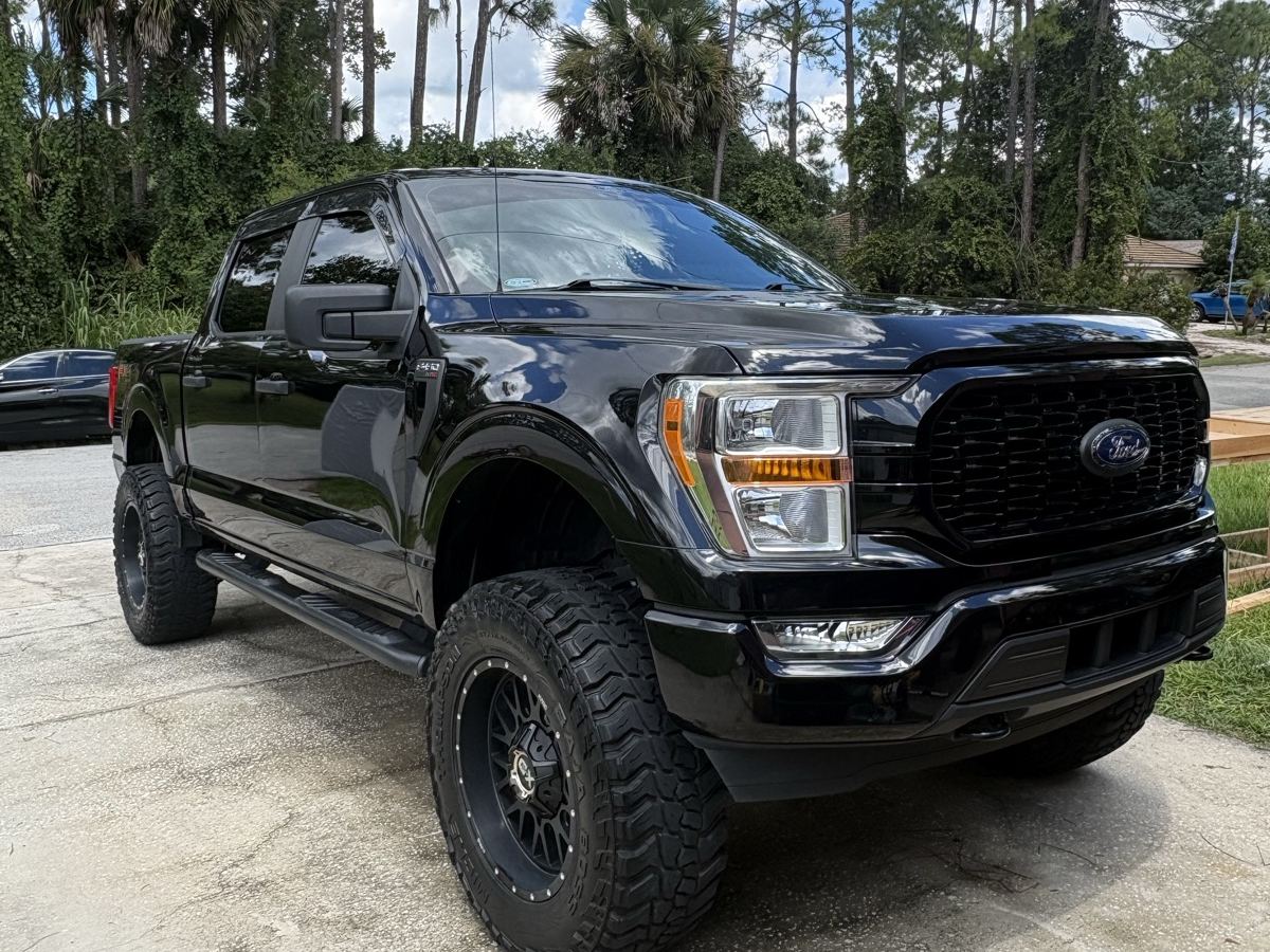 Lifted black Ford F-150 detailed on a driveway under pine trees