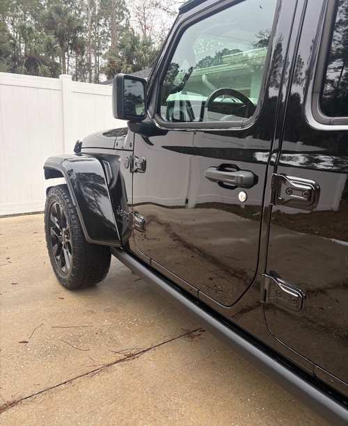 The same black Jeep Gladiator after a multi-step foam wash — paint reflecting the fence line, tires dressed