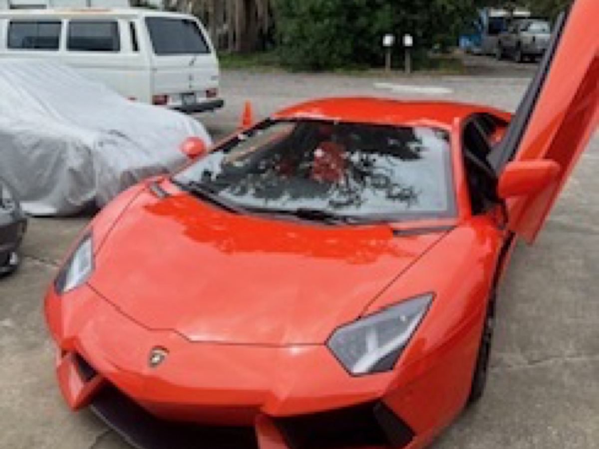 Orange Lamborghini Aventador with its scissor door up after a detail