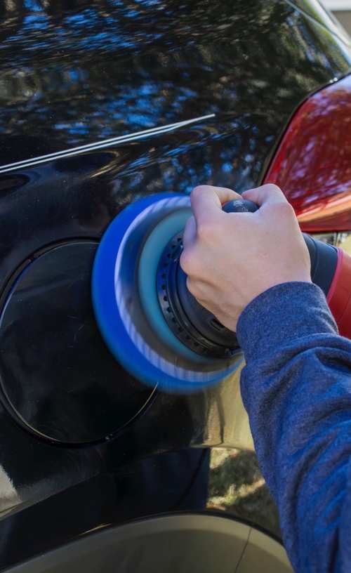 Dual-action polisher with a blue pad working a red panel during paint correction