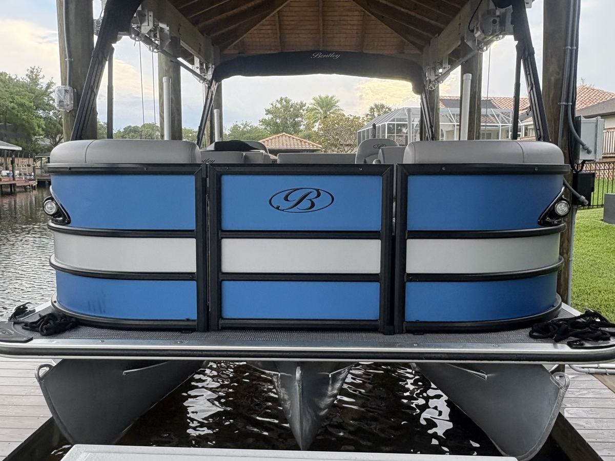 Blue and white Bennington pontoon boat detailed on its lift under a boathouse