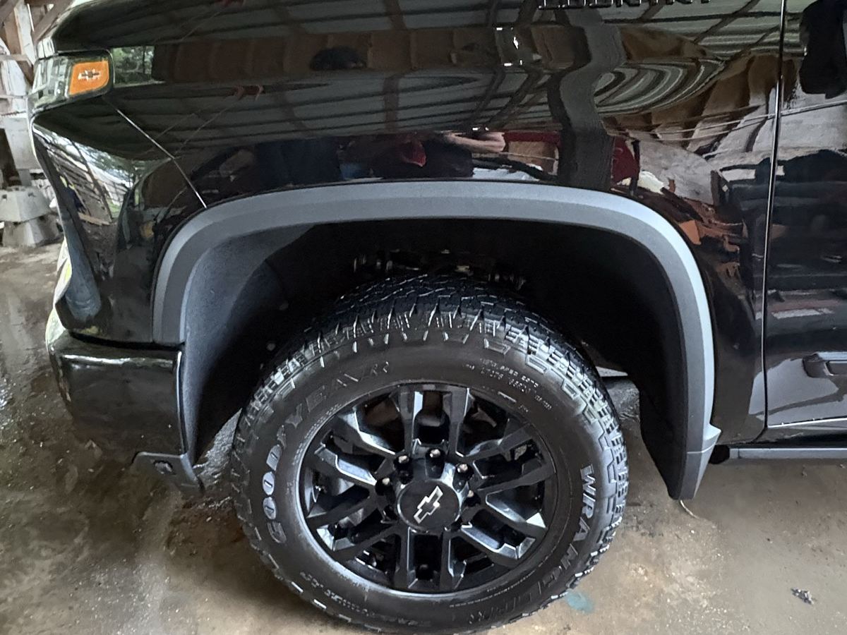 The same Silverado front wheel after a wash — tire dressed, wheel black, fender flare glossy