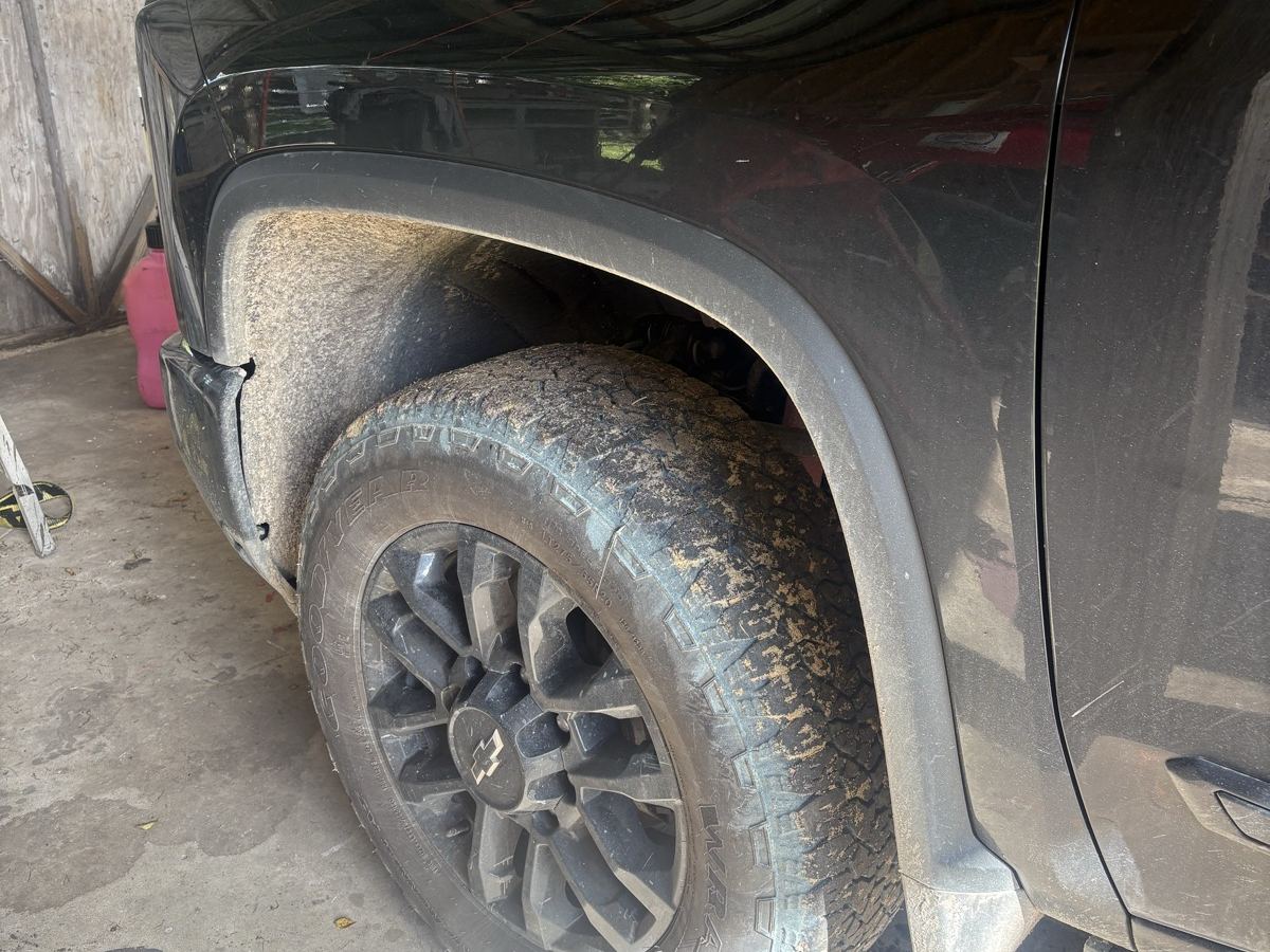 Black Chevy Silverado High Country front wheel before washing — tire and fender caked in dried mud